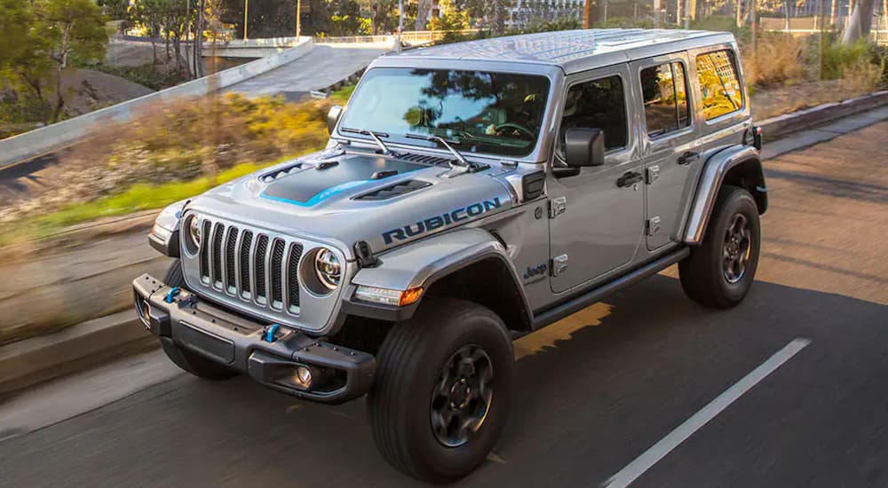 A silver 2021 Jeep Wrangler 4xe driving on a city street near a Jeep dealer.