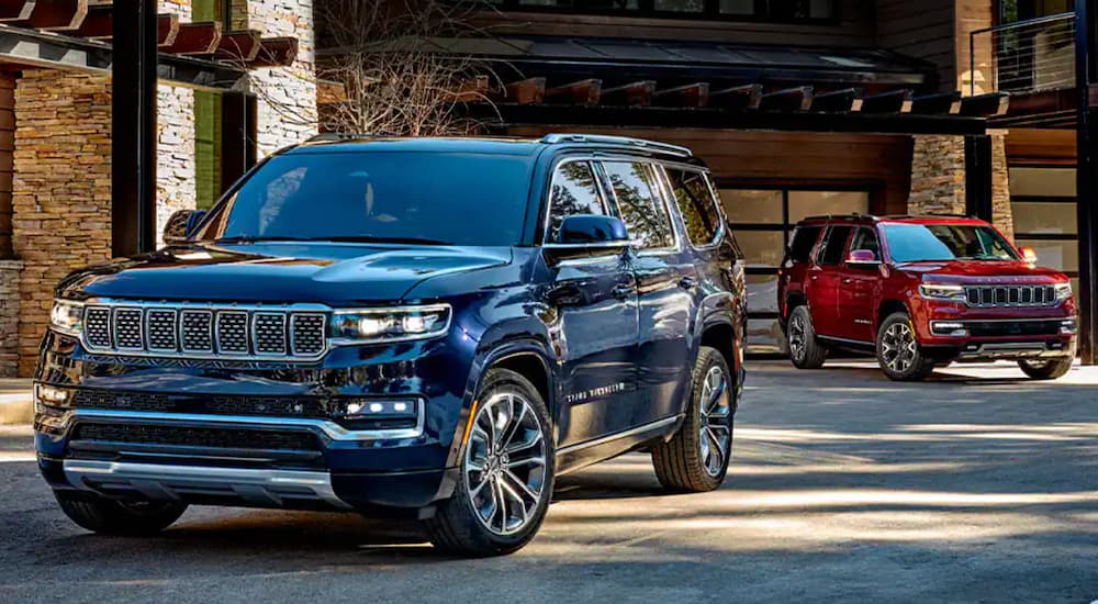A blue and a red 2022 Grand Wagoneer parked in front of a cabin.