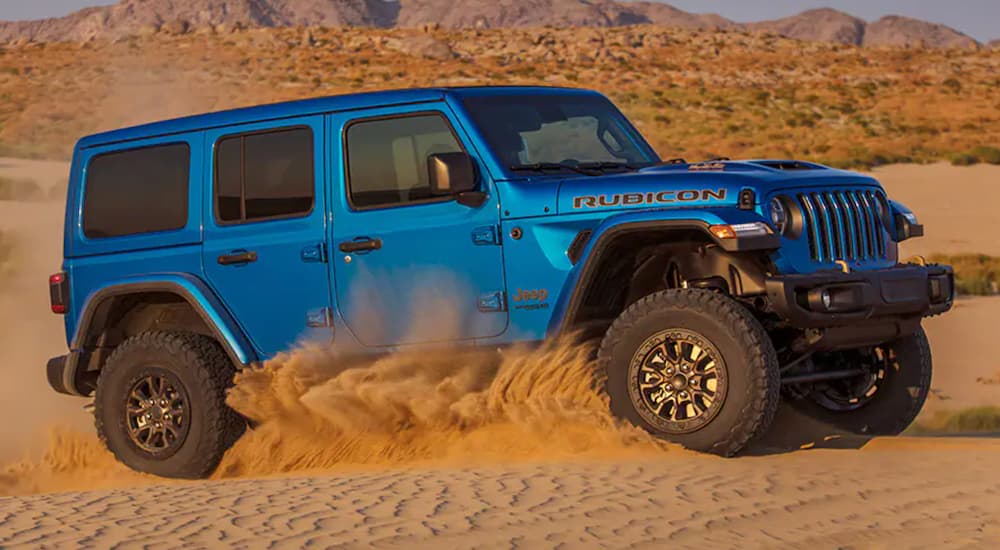 A blue 2021 Jeep Wrangler Unlimited Rubicon 392 kicking up sand while off-roading in the desert.