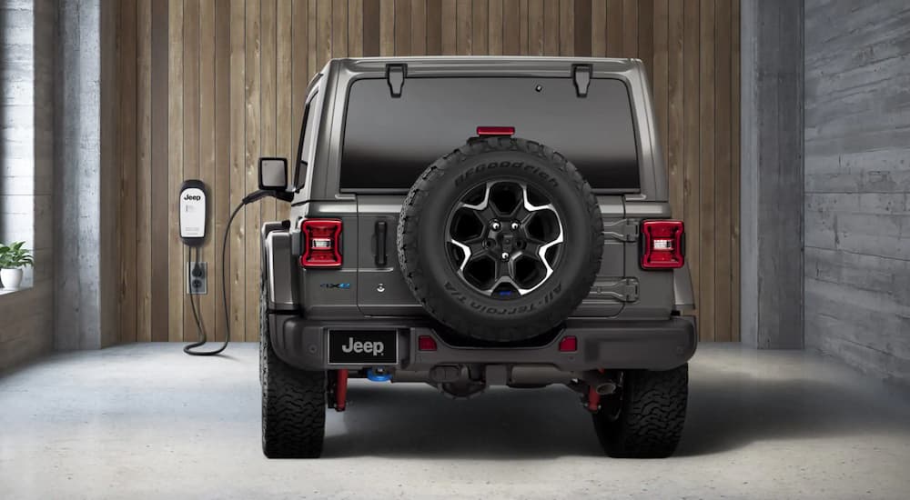 Rear view of a grey 2022 Jeep Wrangler 4xe plugged into an electric vehicle charger in a residential garage.