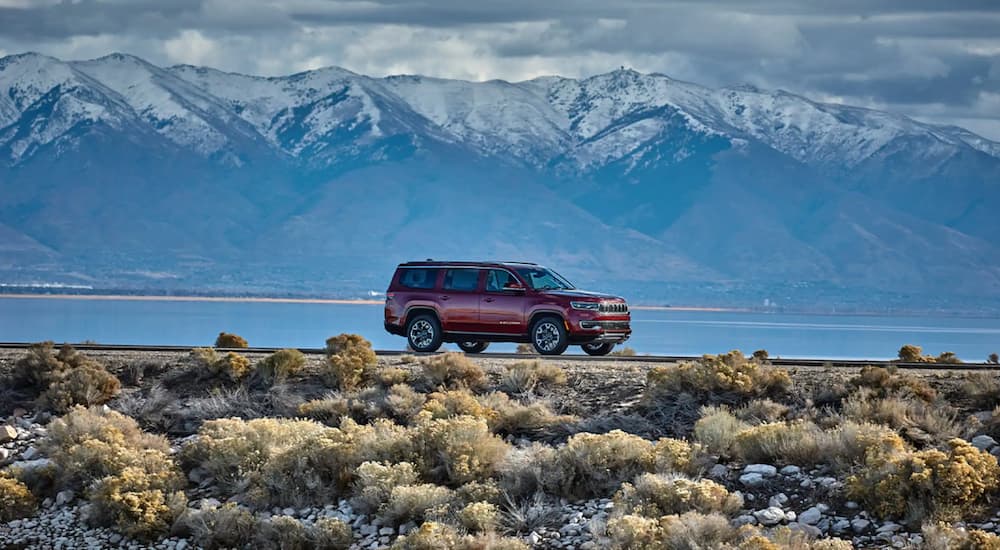 A red 2022 Wagoneer driving on an open road with large snow-capped mountains in the background.