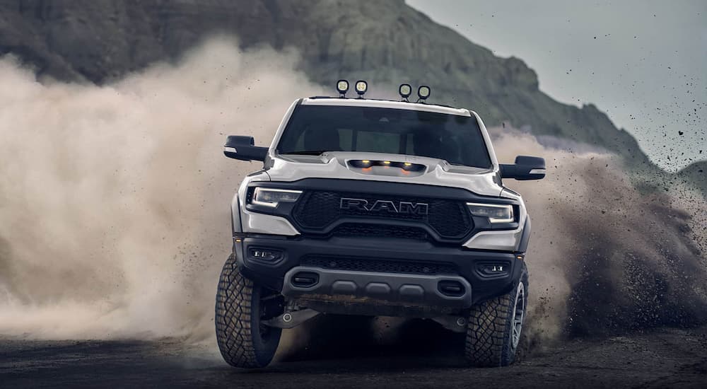 A white 2022 Ram 1500 TRX kicks up dust while off-roading on a sandy trail.