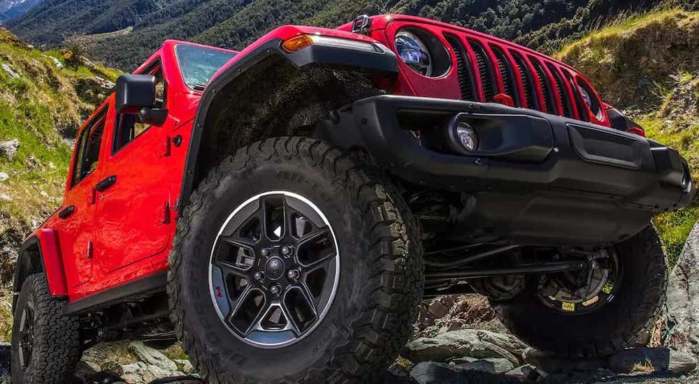 Seen from an extreme low angle, a red 2022 Jeep Wrangler is parked on a rocky hill.