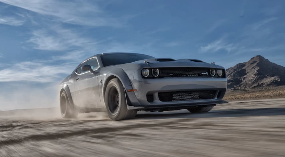 A grey 2022 Dodge Challenger SRT kicking up dust as it drives through an open desert.