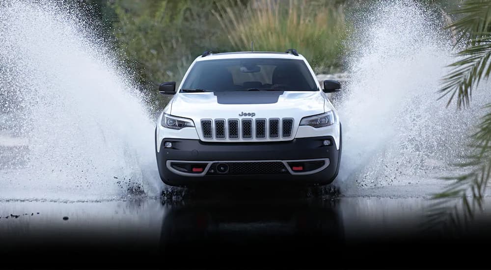 Front-view of a white 2022 Jeep Cherokee Trailhawk splashing through water.