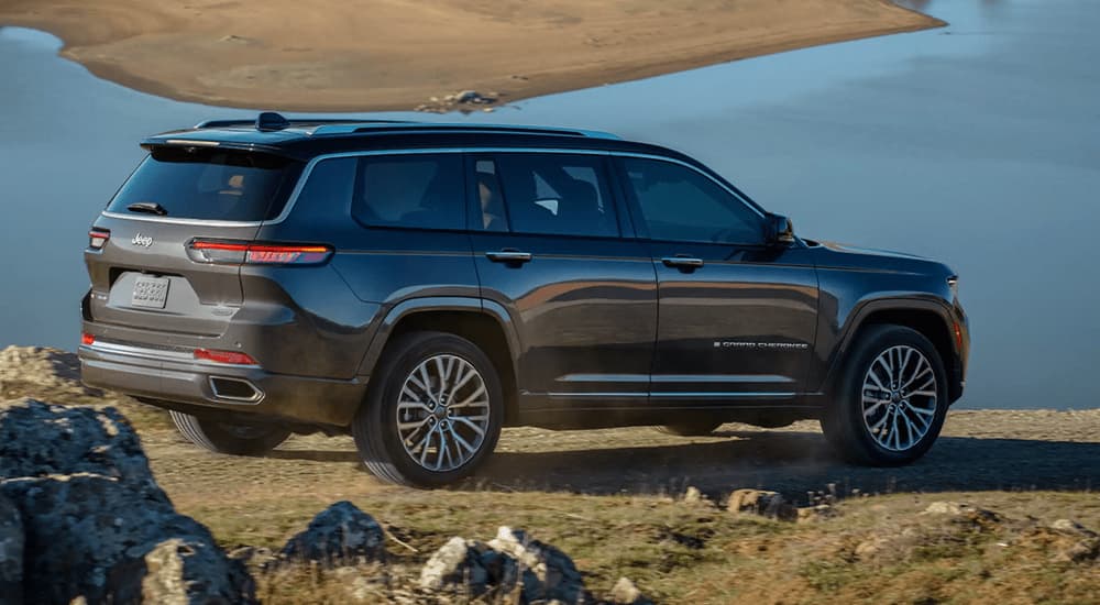 A grey 2022 Jeep Grand Cherokee L parked on a hill overlooking a lake.