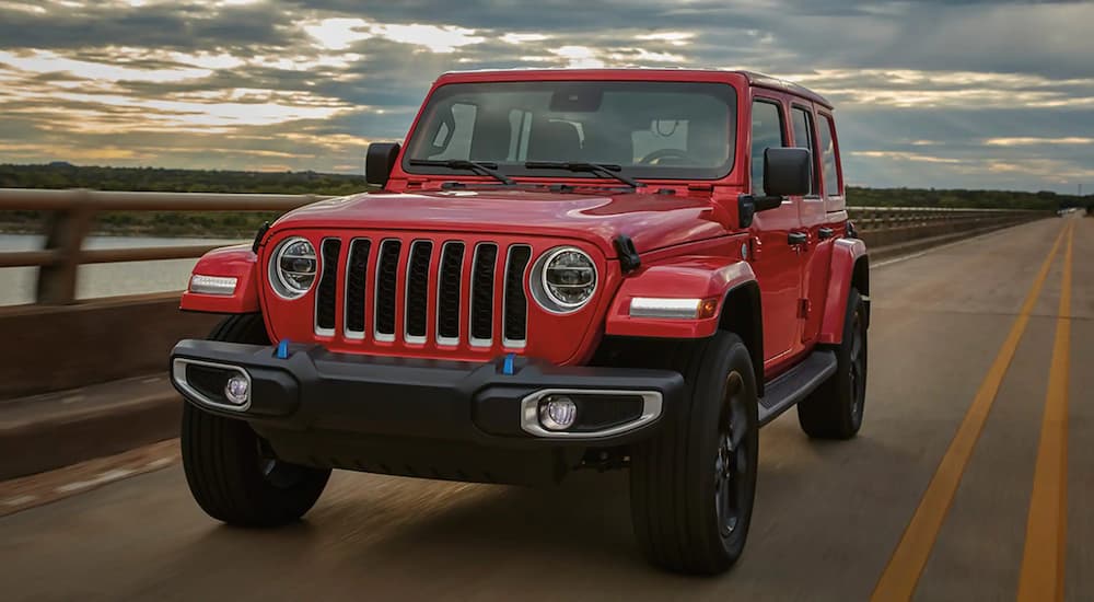 A red 2023 Jeep Wrangler for sale near you is shown from the front driving on an open road.