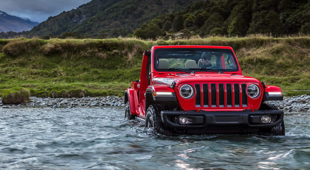 A red 2023 Jeep Wrangler driving through a river.