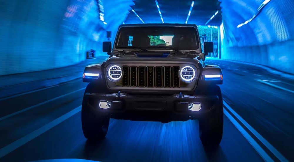 A silver 2024 Jeep Wrangler Rubicon 4xe driving through a blue-illuminated tunnel