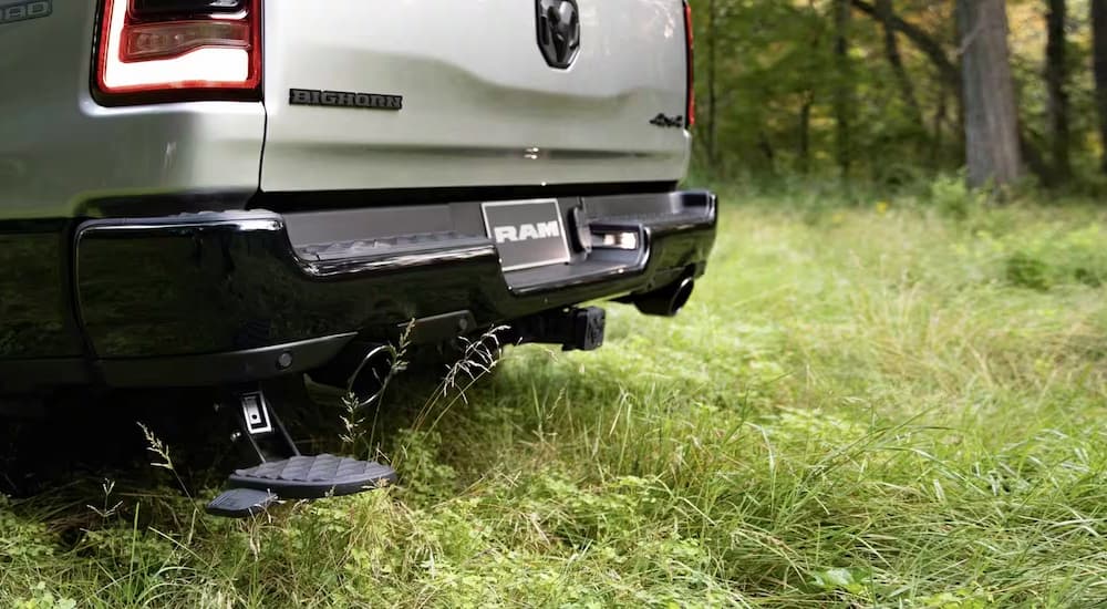 A close up of the rear bumper of a silver 2023 Ram 1500 Big Horn parked in a grassy meadow.