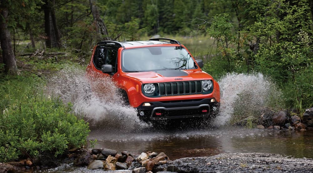 A red 2020 Jeep Renegade splashing through water while off-roading.