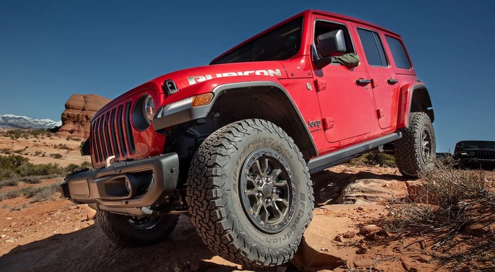 A red 2022 Jeep Wrangler Rubicon off-roading over uneven terrain in the desert.