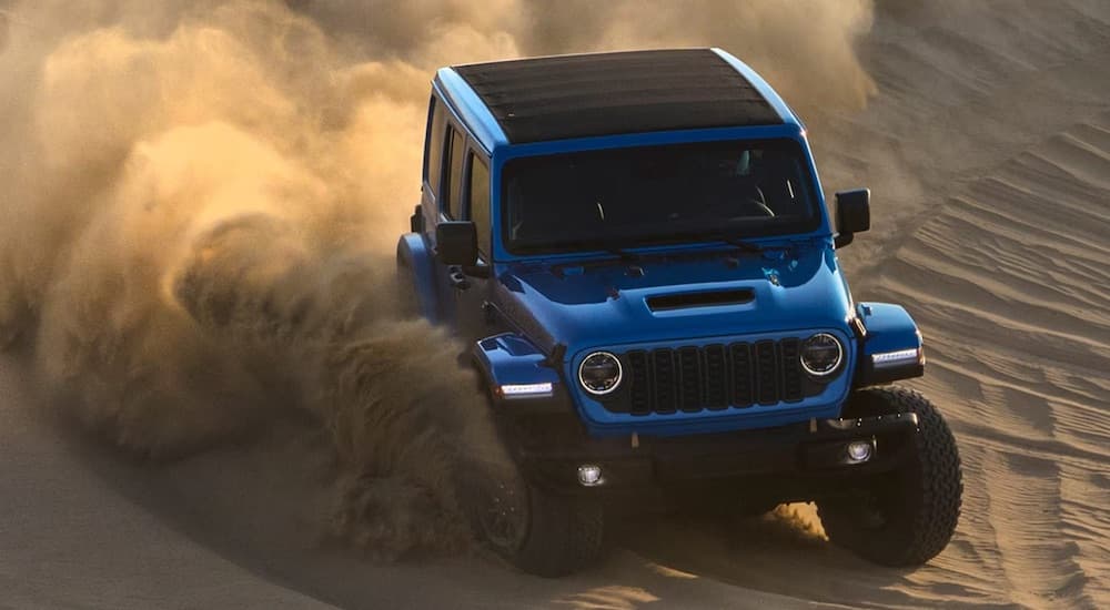 A blue 2021 Jeep Wrangler Rubicon 392 kicking up sand while off-roading through the desert.