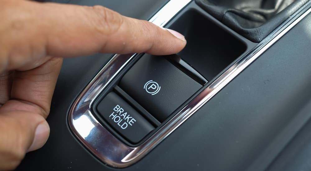 A close up of a hand using an electronic parking brake is shown.