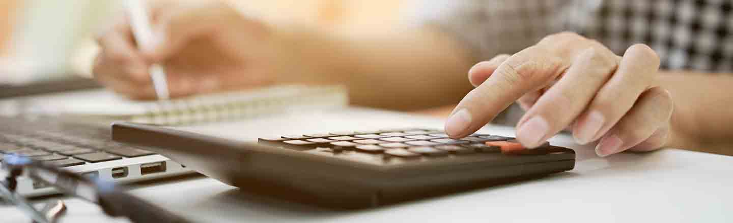 Close up of hands filling out a finance application with laptop, calculator, and notebook
