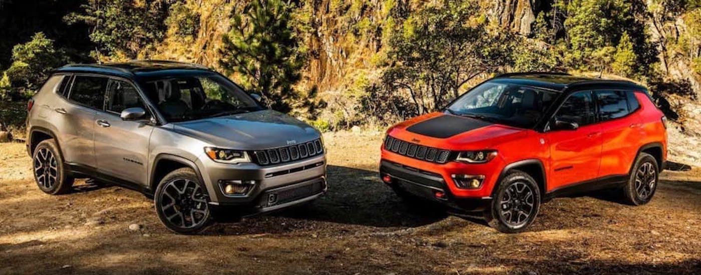 A grey and a red 2018 Jeep Compass are shown parked inward in the mountains.