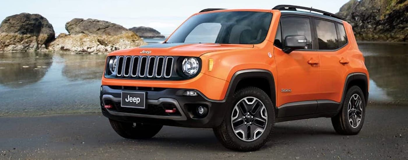 An orange 2018 Jeep Renegade is shown parked in front of a body of water.