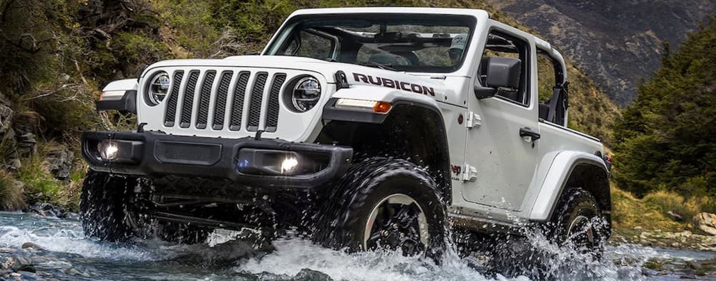 A popular Certified Pre-Owned Jeep, a white 2018 Jeep Wrangler Unlimited Rubicon, is shown off-roading through a river.