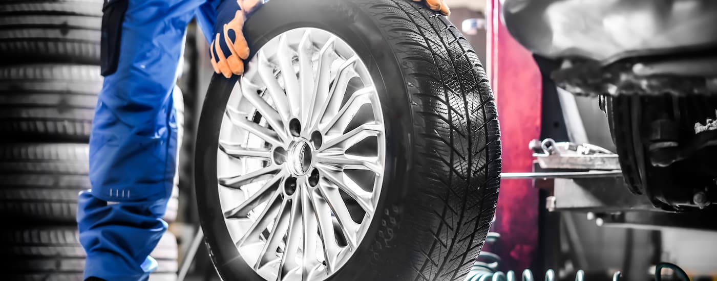 A mechanic is shown standing with a tire on a rim at a repair shop.