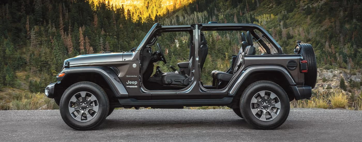 A grey 2022 Jeep Wrangler Sahara is shown from the side parked near the mountains.