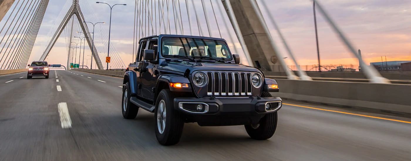 A black 2023 Jeep Wrangler is shown driving on a bridge.