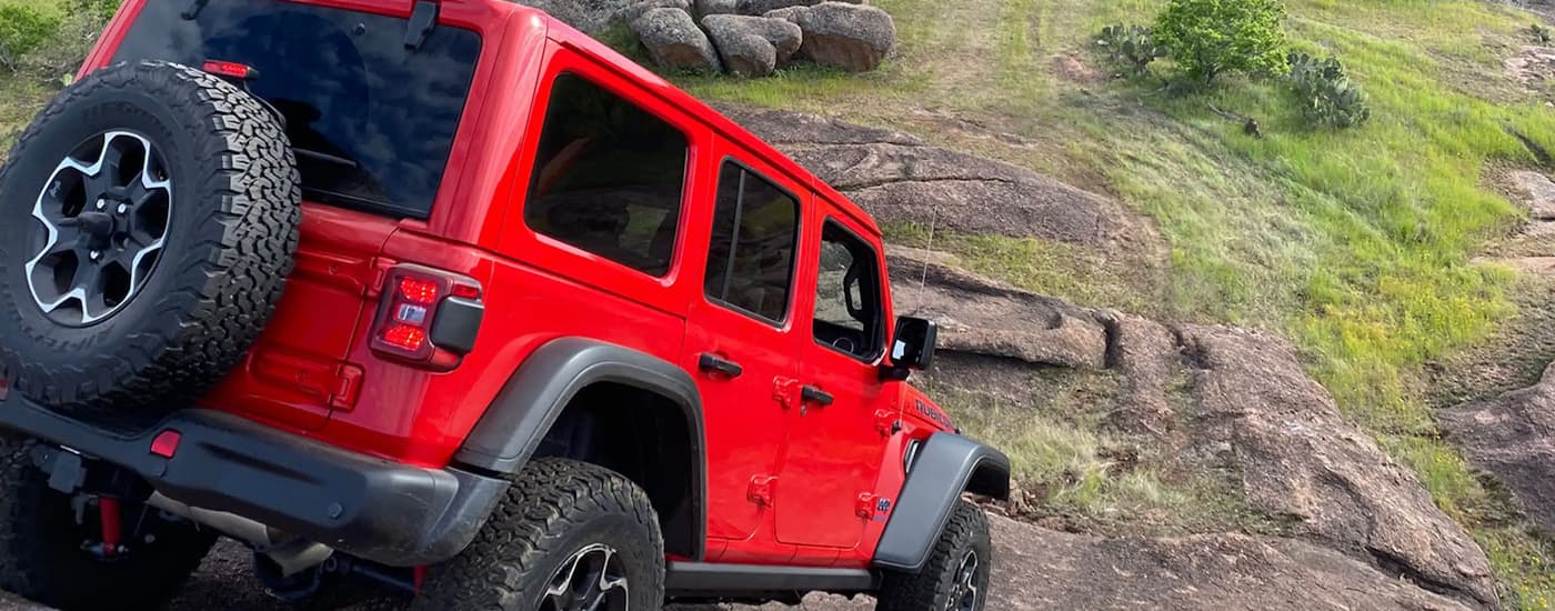 A red 2023 Jeep Wrangler Rubicon for sale near you is shown off-roading down a steep rocky trail.
