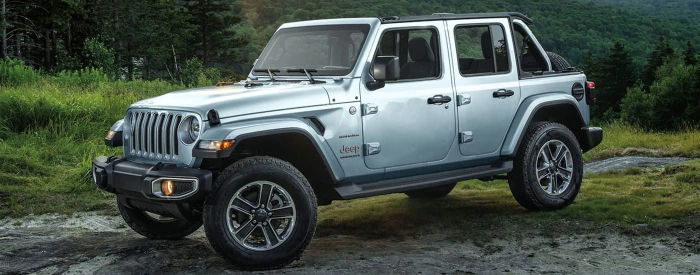 A silver 2023 Jeep Wrangler Sahara is shown from the side parked on a trail.