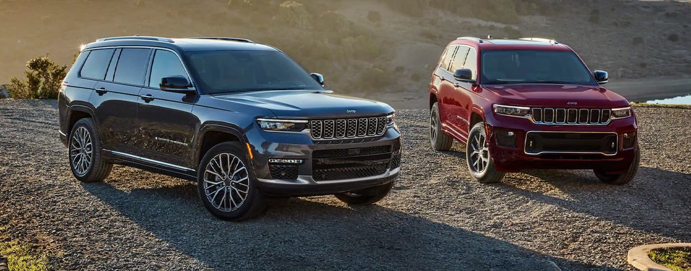 A black and a red 2021 Jeep Grand Cherokee L are parked on gravel.