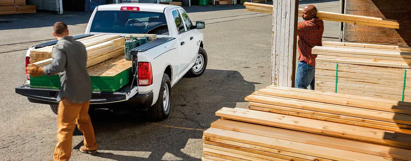 A white 2017 Ram 1500 is shown from the rear while lumber is loaded in the bed.