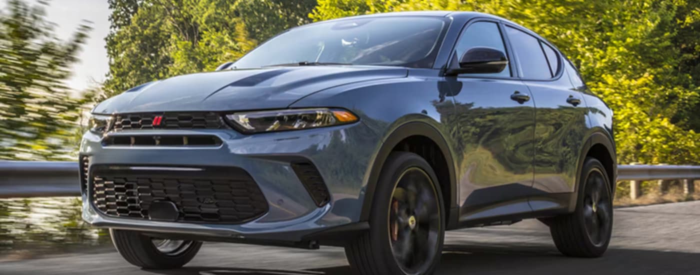 A blue-grey 2023 Dodge Hornet is shown from a front angle while driving next to a guardrail.