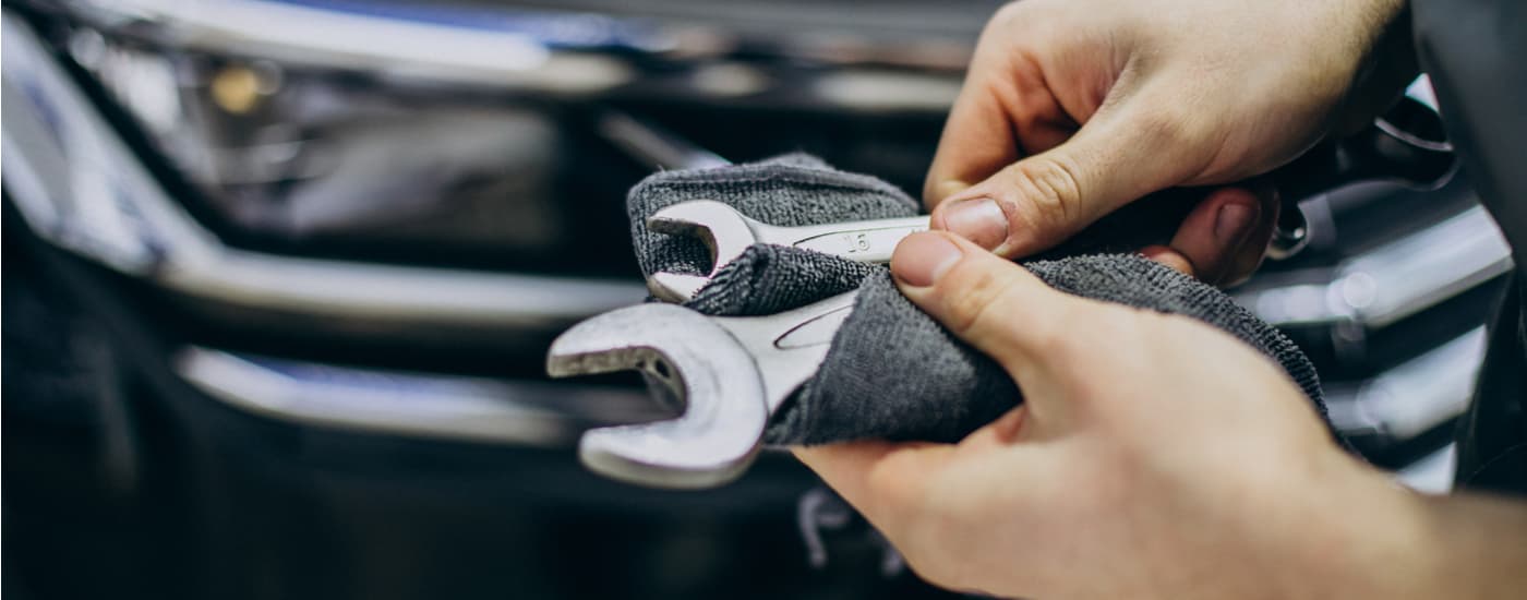 A mechanic is shown holding tools in front of a black SUV.